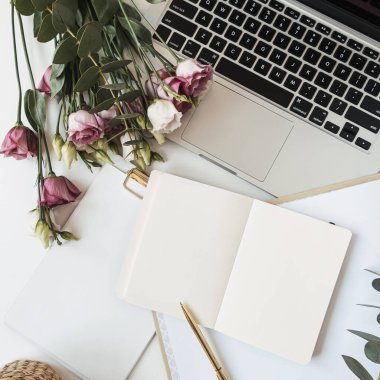 Ev hanımı, patroniçenin çalışma odası, boş bir not defteri, dizüstü bilgisayarı, güller, çiçek buketi, okaliptüs dalı beyaz masa. Ev işlerinde üst düzey çalışma, dış kaynak kullanımı kavramı.