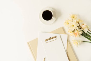Not panosu, kırtasiyesi ve narsisli çiçekleri olan güzel modern ofis çalışma alanı. Flatlay, üst düzey minimalist çalışma masası. Taklit alanı olan boş sayfa kağıdı