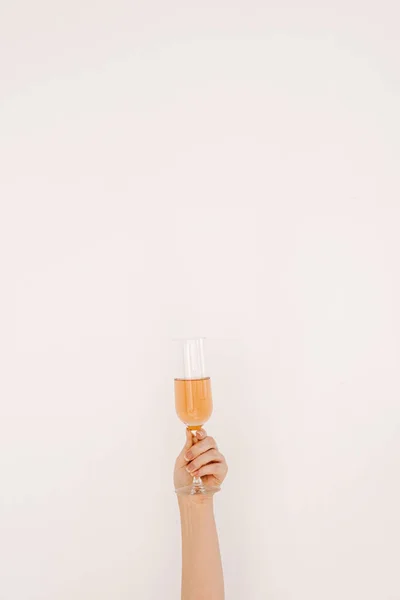 Cheers! Women\'s hand holding glass of rose champagne against white wall. Happy Birthday, anniversary party celebrating decoration festive concept