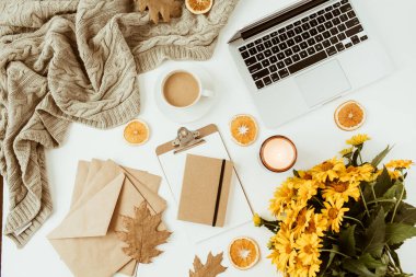 Laptop, dosya, çiçek buketi, kahve fincanı, battaniye, zarflar, yapraklar, beyaz arka planda portakal dilimleri olan düz bir ofis masası çalışma alanı. Üst düzey kadın patron işi, iş konsepti.