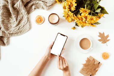 Kadınlar cep telefonlarını tutarlar. Ofis masası çalışma alanı. Düzlük, üst düzey kız patron iş konsepti. Battaniye, çiçek buketi, yapraklar, kahve fincanı. Sosyal medya şablonu.