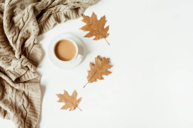 Sütlü kahve, bej örgü ekose, beyaz arka planda kuru yapraklar. Düz yerde, üst tarafta. En düşük sonbahar sabahı kahvaltı kompozisyonu.
