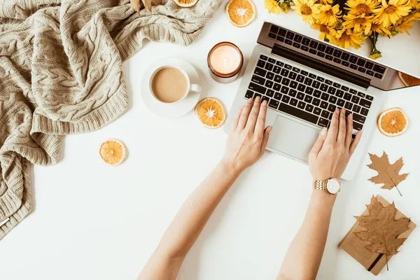 Kadın dizüstü bilgisayarda çalışıyor. Ofis masası çalışma alanı. Düz yatış, üst düzey bayan patron iş konsepti. Klavyede kadın eli var. Battaniye, çiçek buketi, yapraklar, beyaz arka planda kahve fincanı.