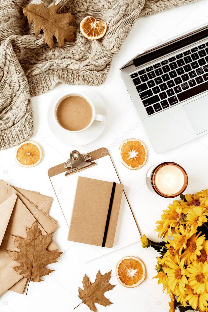 Flat lay home office table desk workspace with laptop, clipboard, flowers bouquet, coffee cup, blanket, envelopes, leaves, orange slices on white background. Top view girl boss business, work concept.