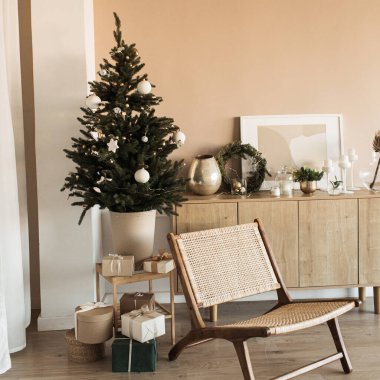 Oyuncaklarla, mücevherlerle ve ev yapımı kağıt hediye kutularıyla güzel bir Noel ağacı. Noel / Yeni Yıl kutlaması için dekore edilmiş oturma odası. Rattan sandalyeli, bej renkli duvarlı modern iç tasarım konsepti.