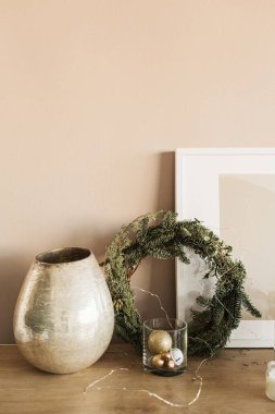 Noel çelengi çerçevesi, altın mücevherler, vazo, bej duvarda çerçeve. Minimalist ev dekorasyonu konsepti. Noel, Yeni Yıl Tatil Kutlamaları.
