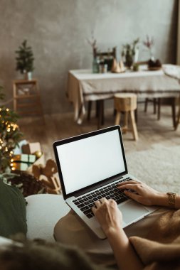 Genç bir kadın dizüstü bilgisayarda çalışıyor. Boş ekran ve taklit alanı var. Modern ev oturma odası iç tasarımı. Noel, Yeni Yıl Kompozisyonu.