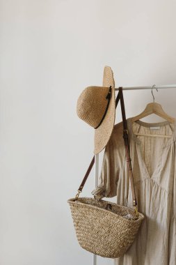 Hasır şapka, saman el çantası, beyaz duvarın üzerinde asılı bej keten elbise.