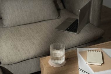 Ev ofisinin çalışma odası rahat koltukta dizüstü bilgisayarı var. Not defteri, bir bardak su. Sabah işi, iş konsepti. Masada güneş ışığı gölgeleri