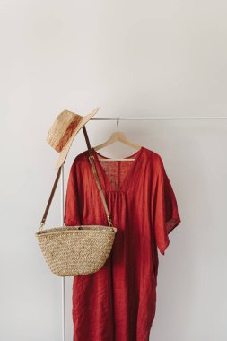 Hasır şapka, saman çanta, kırmızı elbise beyaz duvarın üzerinde askılık.