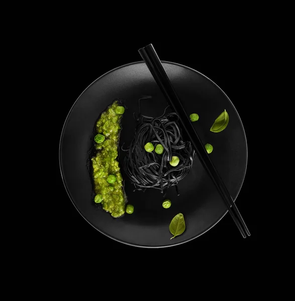 plate of black noodles with green peas and chopsticks