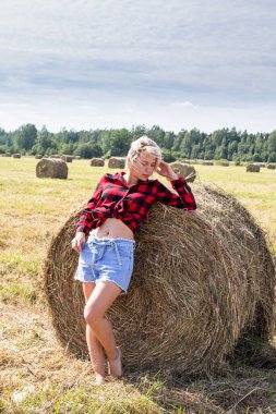 Genç bir kadın saman balyasında oturuyor.