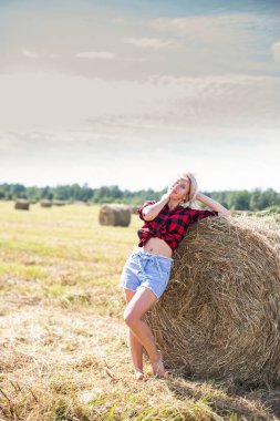 Genç bir kadın saman balyasında oturuyor.