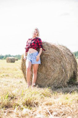 Genç bir kadın saman balyasında oturuyor.