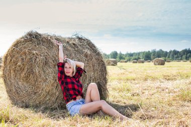 Genç bir kadın saman balyasında oturuyor.