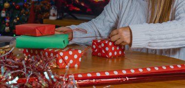 Noel Baba şapkalı kadın süslenmiş ağaç ve şöminenin yanında Noel hediyelerini paketliyor bayram kutlaması için hediyeler hazırlıyor.