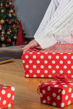 Beyaz kazaklı kadın Noel hediyesini süslenmiş ağaç ve şöminenin yanındaki kırmızı benekli kağıda sarıyordu.