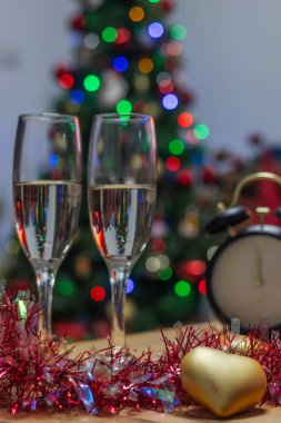 Şöminenin önündeki şenlik masasında şişe ve saatle birlikte iki şampanya bardağı. Yeni yıl kutlamasını ve gece yarısı geri sayımını simgeliyor.