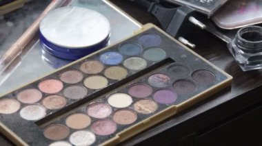 Young woman holding multicolor palette of eyeshadows in hand while make up artist work with her face. Closeup of colourful professional set of eye shadows for beautiful make-up.