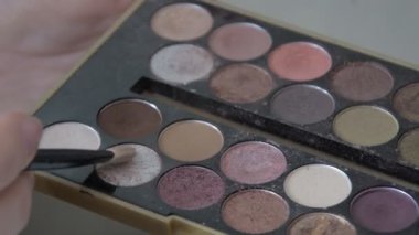Young woman holding multicolor palette of eyeshadows in hand while make up artist work with her face. Closeup of colourful professional set of eye shadows for beautiful make-up.