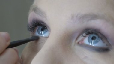 Kız mavi gözler için profesyonel makyaj yapar. Özel bir fırça kullanarak gözü siyahla çevreler. Bu gözleri daha anlamlı hale getirir