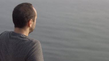 Genç adam deniz - üzerinden seyir uçurumun kenarına oturur omuz