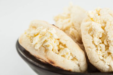 Kolombiyalı geleneksel beyaz Mısır arepa beyaz arka plan üzerinde siyah bir seramik tabak içinde rendelenmiş peynir ile doldurulmuş