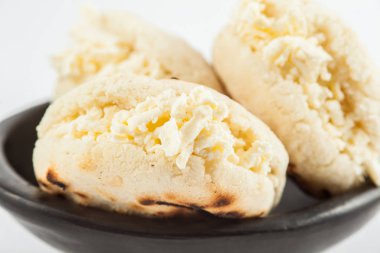 Kolombiyalı geleneksel beyaz Mısır arepa beyaz arka plan üzerinde siyah bir seramik tabak içinde rendelenmiş peynir ile doldurulmuş