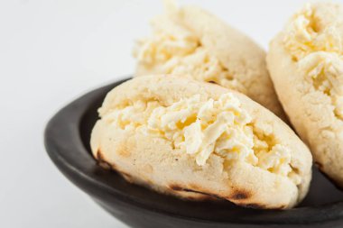 Kolombiyalı geleneksel beyaz Mısır arepa beyaz arka plan üzerinde siyah bir seramik tabak içinde rendelenmiş peynir ile doldurulmuş