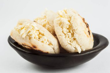 Kolombiyalı geleneksel beyaz Mısır arepa beyaz arka plan üzerinde siyah bir seramik tabak içinde rendelenmiş peynir ile doldurulmuş