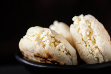Kolombiyalı geleneksel beyaz Mısır arepa siyah arka plan üzerine siyah bir seramik tabak içinde rendelenmiş peynir ile doldurulmuş