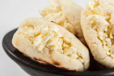 Kolombiyalı geleneksel beyaz Mısır arepa beyaz arka plan üzerinde siyah bir seramik tabak içinde rendelenmiş peynir ile doldurulmuş
