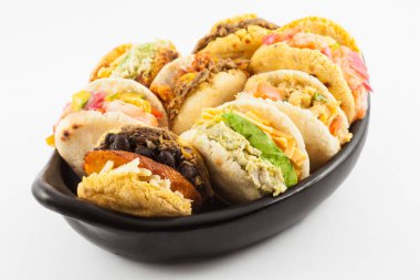 Arepas with assorted fillings served in a black ceramic dish on white background clipart