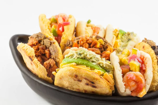 Beyaz arka plan üzerinde siyah bir seramik tabak arepas çeşitli dolguları ile servis