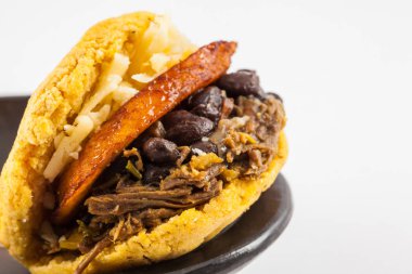 Arepas filled with shredded beef, black beans, plantain and cheese served in a black ceramic dish on white background clipart