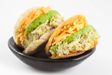 Beyaz arka plan üzerinde siyah bir seramik tabak içinde parçalanmış tavuk ve avokado dolu Arepas hizmet