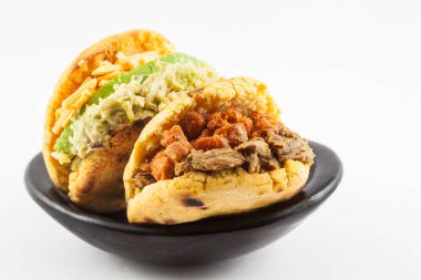 Arepas with two different fillings served in a black ceramic dish on white background clipart