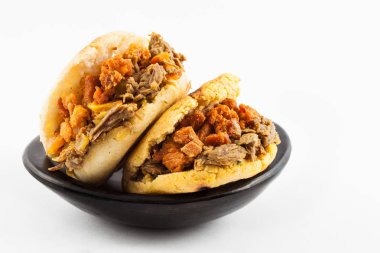 Beyaz arka plan üzerinde siyah bir seramik tabak içinde parçalanmış sığır eti ve domuz eti kabuklu dolu Arepas hizmet
