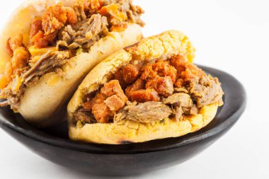 Beyaz arka plan üzerinde siyah bir seramik tabak içinde parçalanmış sığır eti ve domuz eti kabuklu dolu Arepas hizmet