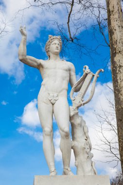 PARIS, FRANCE - MARCH, 2018: Statue of Apollo with a lyre at the garden of the Versailles Palace in a freezing winter day just before spring clipart