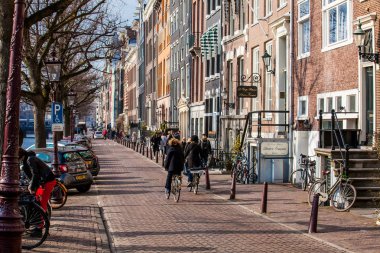 Amsterdam, Hollanda - Mart, 2018: insanlar yürüyüş ve eski Merkez İlçe Amsterdam kanalları yanındaki güzel Arnavut kaldırımlı sokakları, Bisiklet sürme