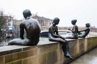 Berlin, Almanya - Mart, 2018: Üç kız ve bir erkek Wilfried Fitzenreiter tarafından oluşturulan heykel Spree Nehri kıyısında yer alan kış günü bir soğuk yağışlı ucunda