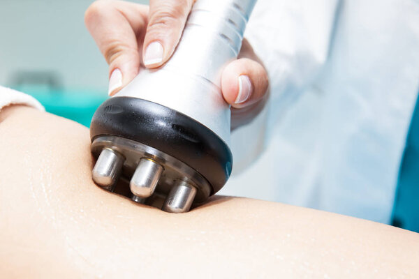 Doctor performing a radiofrequency treatment on a young female patient leg