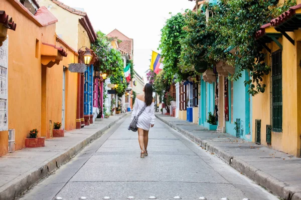 Krásná žena na bílých šatech, která kráčí sama v pestrobarevné ulici koloniálního opevněného města Cartagena de Indias — Stock fotografie