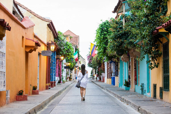Beautiful woman on white dress walking alone at the colorful streets of the colonial walled city of Cartagena de Indias
