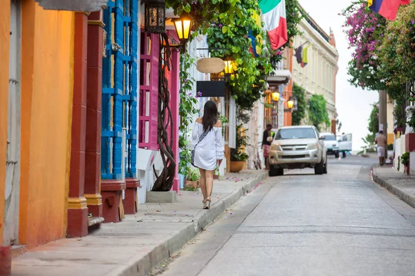 Krásná žena na bílých šatech, která kráčí sama v pestrobarevné ulici koloniálního opevněného města Cartagena de Indias — Stock fotografie