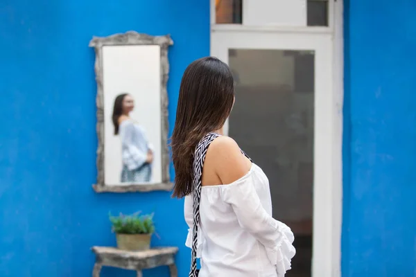 Schöne Frau im weißen Kleid, die sich selbst auf einem Spiegel in den farbenfrohen Straßen der kolonialen ummauerten Stadt Cartagena de Indias betrachtet — Stockfoto
