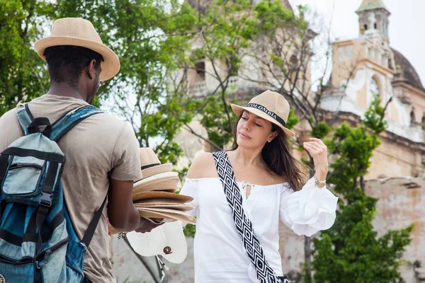 Hermosa joven comprando un sombrero tradicional colombiano a un vendedor ambulante en Cartagena de Indias — Foto de Stock