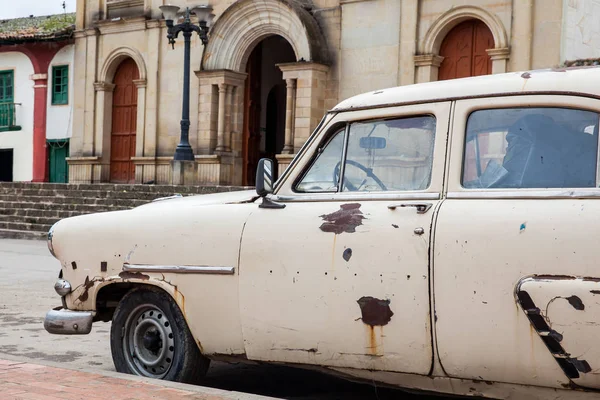 Antique rusty car parked next to the Parish Church of the small town of Ventaquemada in Colombia — Stock Photo, Image