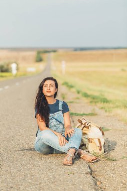 Yol kenarında oturan bir sırt çantası ile kız. macera kavramı.